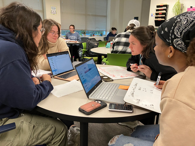 A group of students working together with laptops and whiteboards in the center.